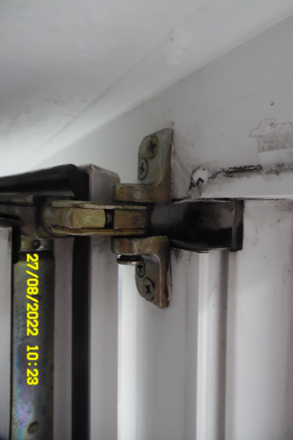 Close-up of a rusty part of a door hinge on a white door frame, screws visible.