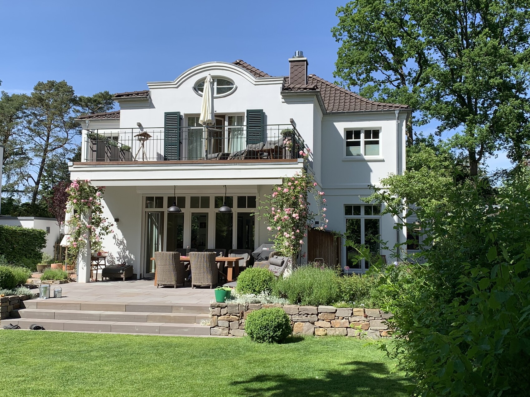 Two-story white house with balcony and outdoor dining area in the garden.