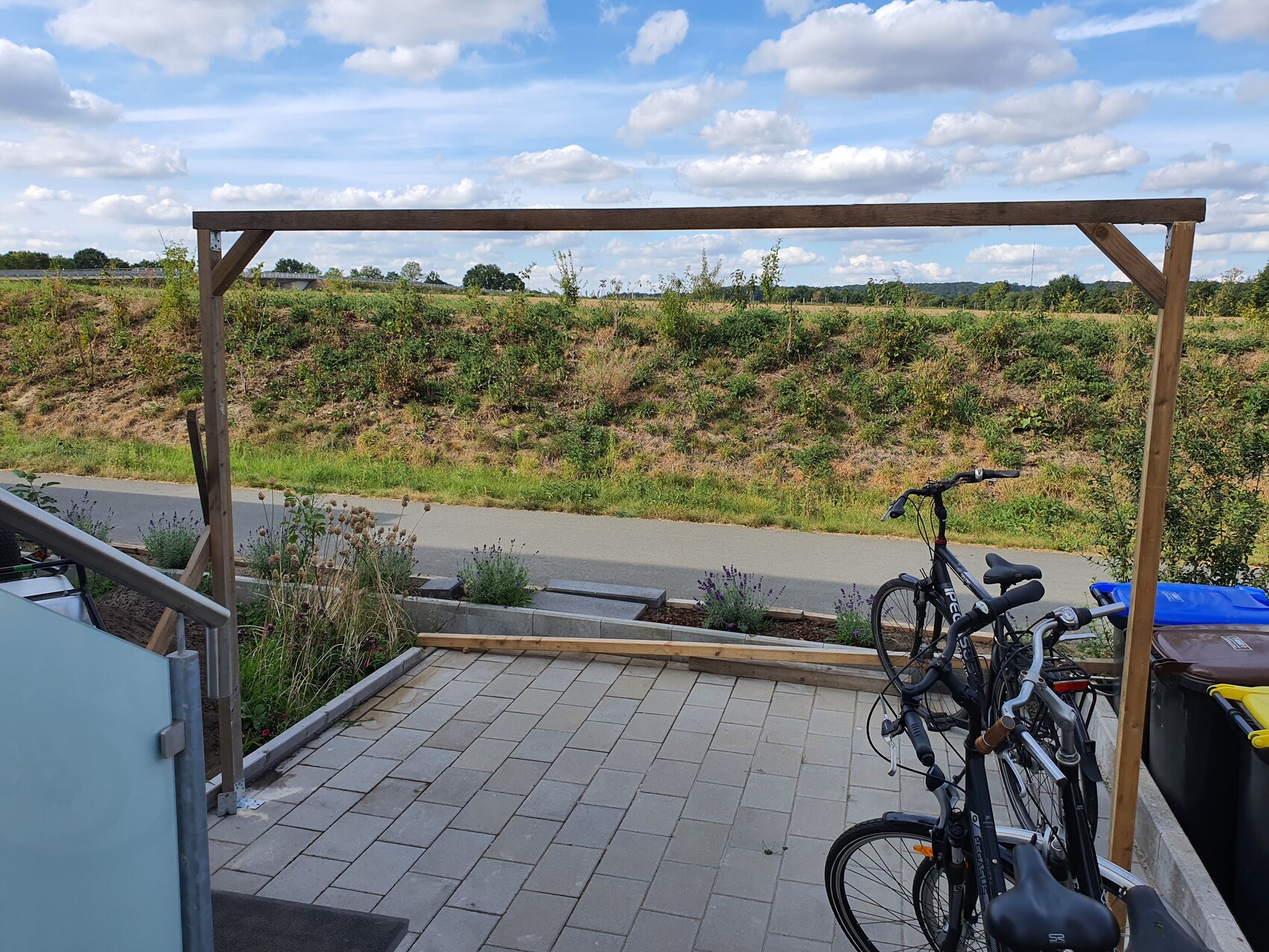 Wooden frame on terrace, bicycles beside it, view of street and green hills.