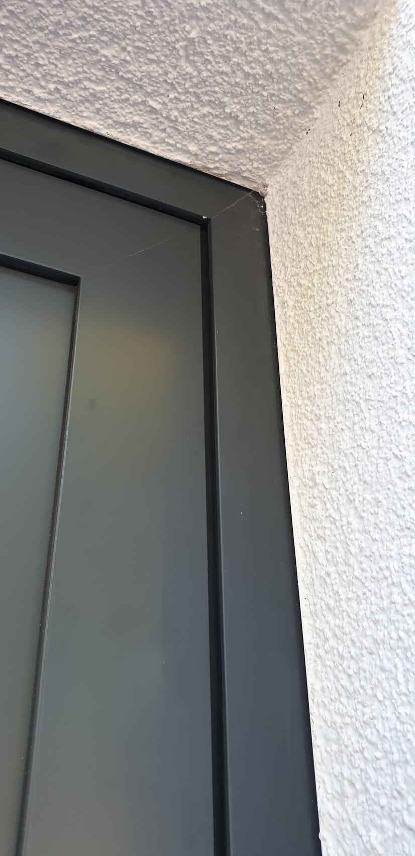 Close-up of a grey metal window frame on a rough white wall, corner visible.