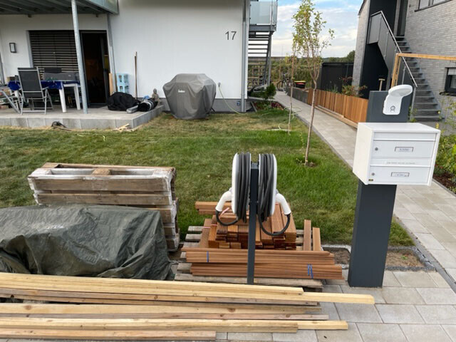 Garden and construction area in front of house no. 17: wooden planks, pallets, hose reel.