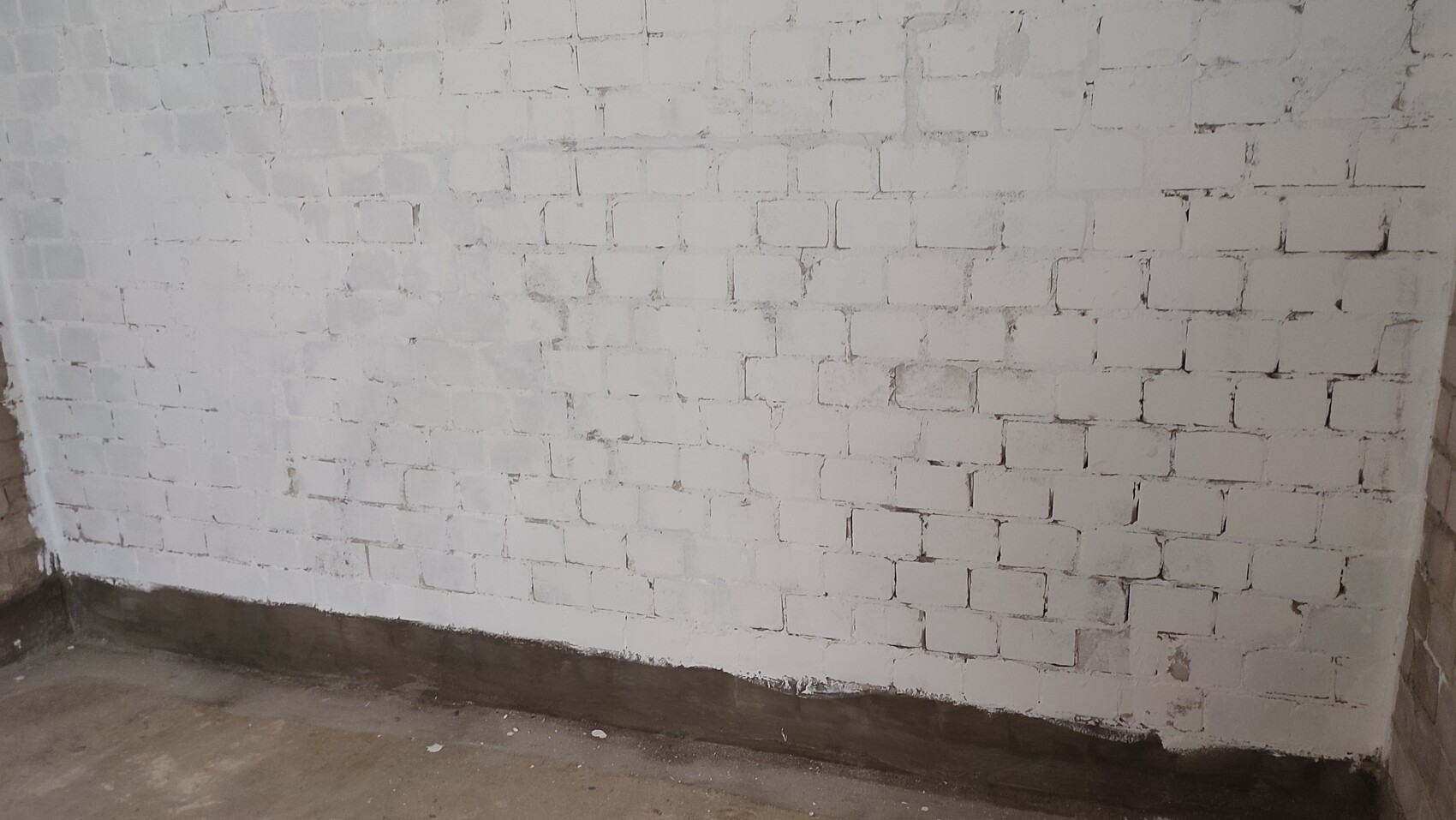 White brick wall in a basement room, with a darker strip near the floor.