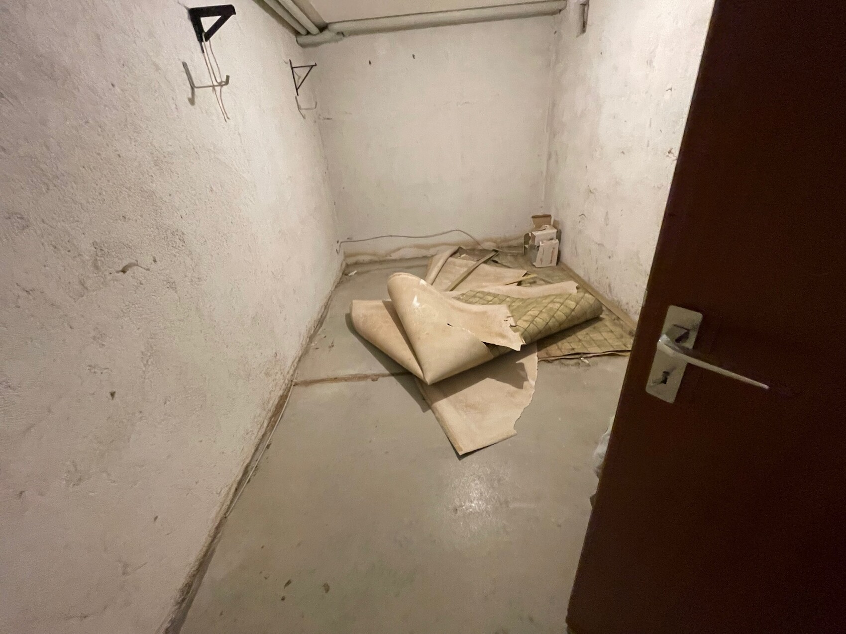 Basement room with rough concrete walls, carpet rolls and boxes on the floor, open door.