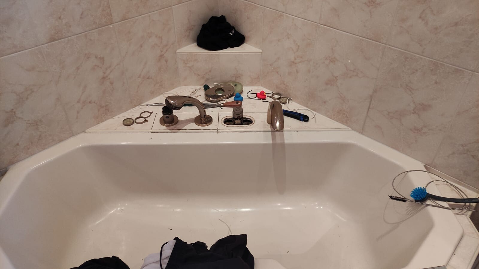 Badewanne mit Armaturen, lose Dichtungen, Kleinteile und blaue Reinigungsbürste; Kleidung am Rand.