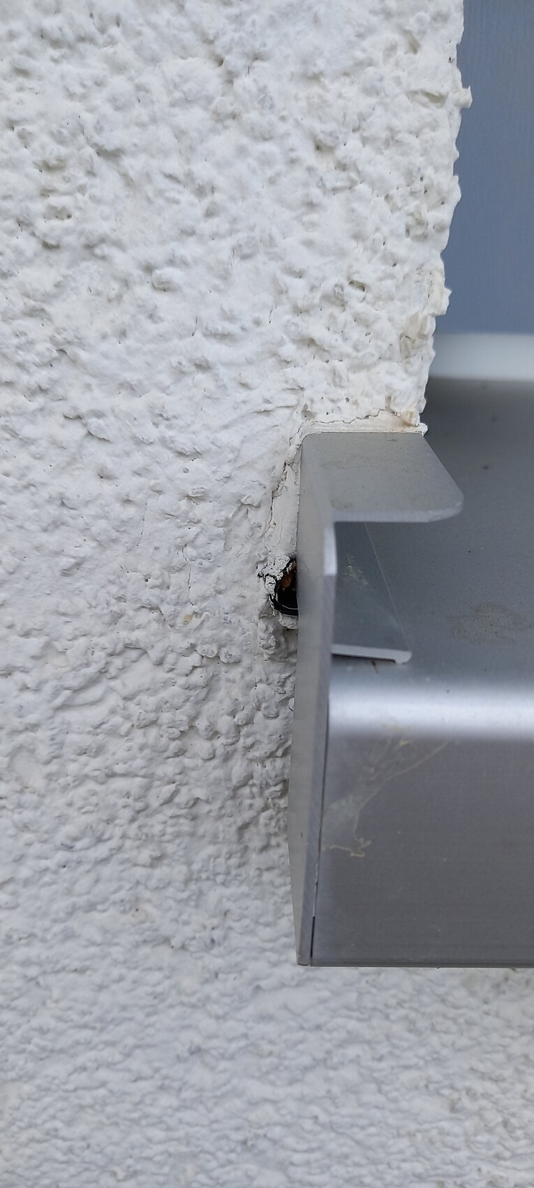 Nahaufnahme einer rauen weißen Putzwand mit einem grauen Metallwinkel, der seitlich herausragt.