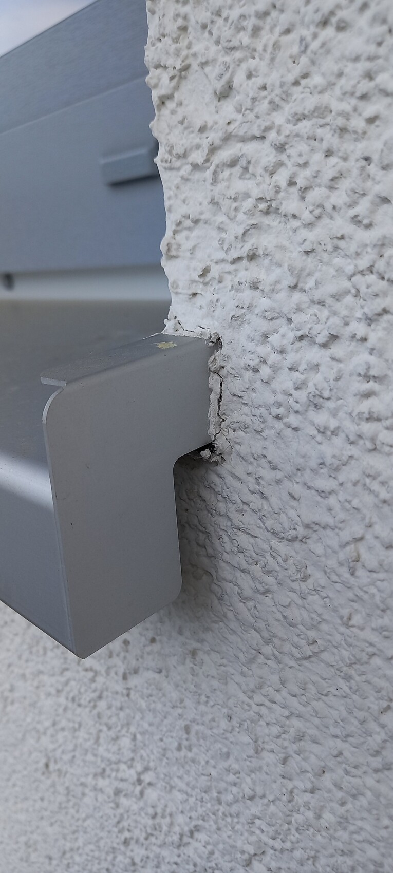Nahaufnahme eines grauen, rechteckigen Außen-Metallgehäuses an rauer weißer Putzwand.
