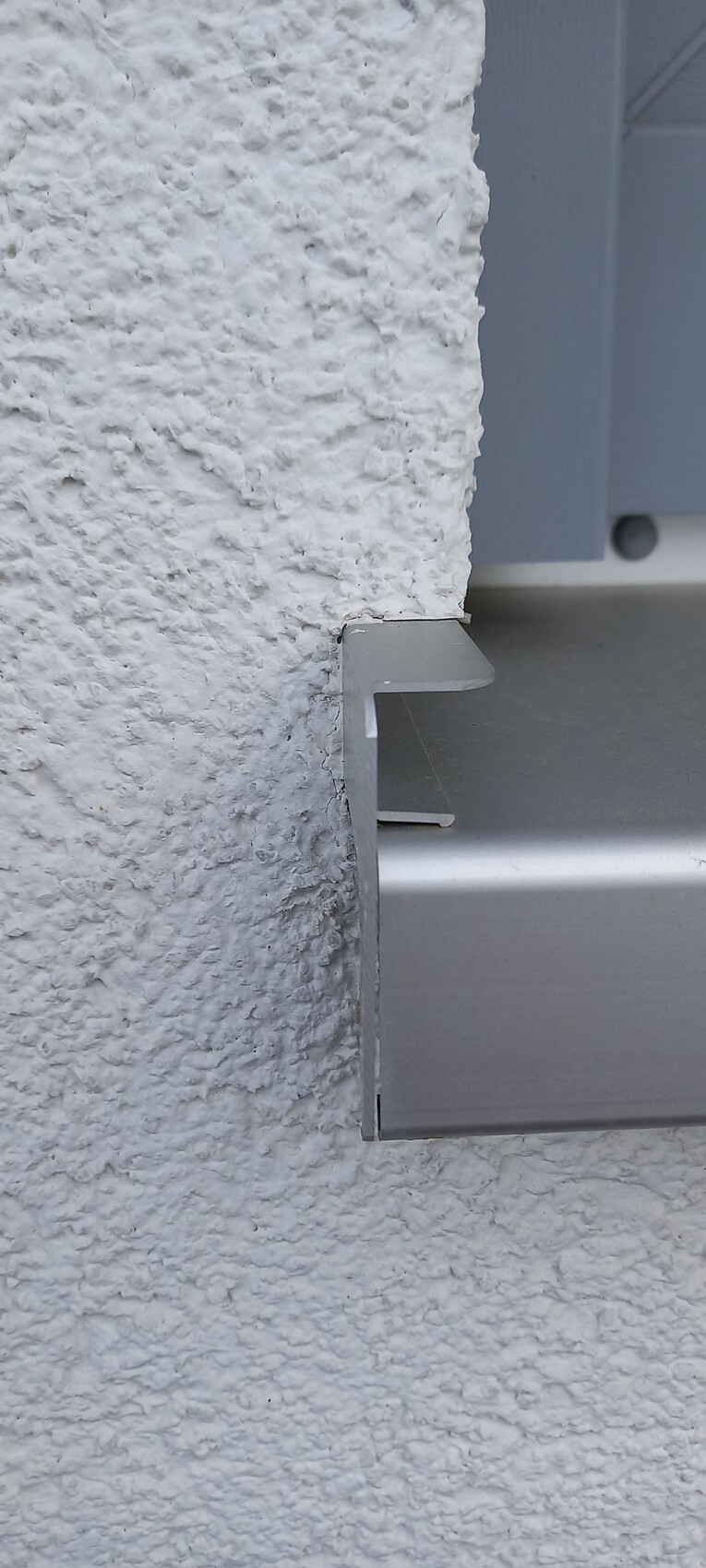 Nahaufnahme einer grauen Metallhalterung an einer rauen weißen Putzwand.