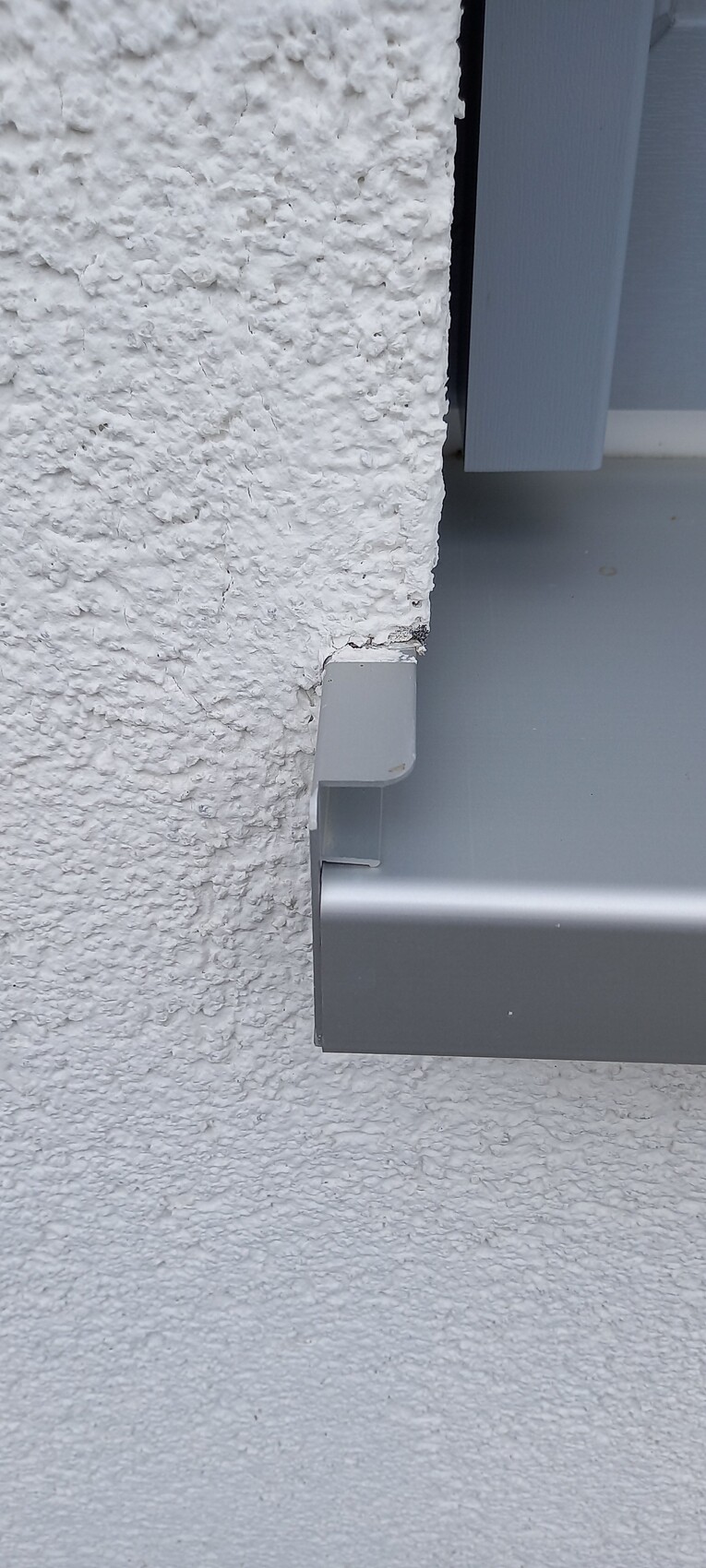 Grobe weiße Außenwand links; graue Metallhalterung ragt horizontal aus der Wand.