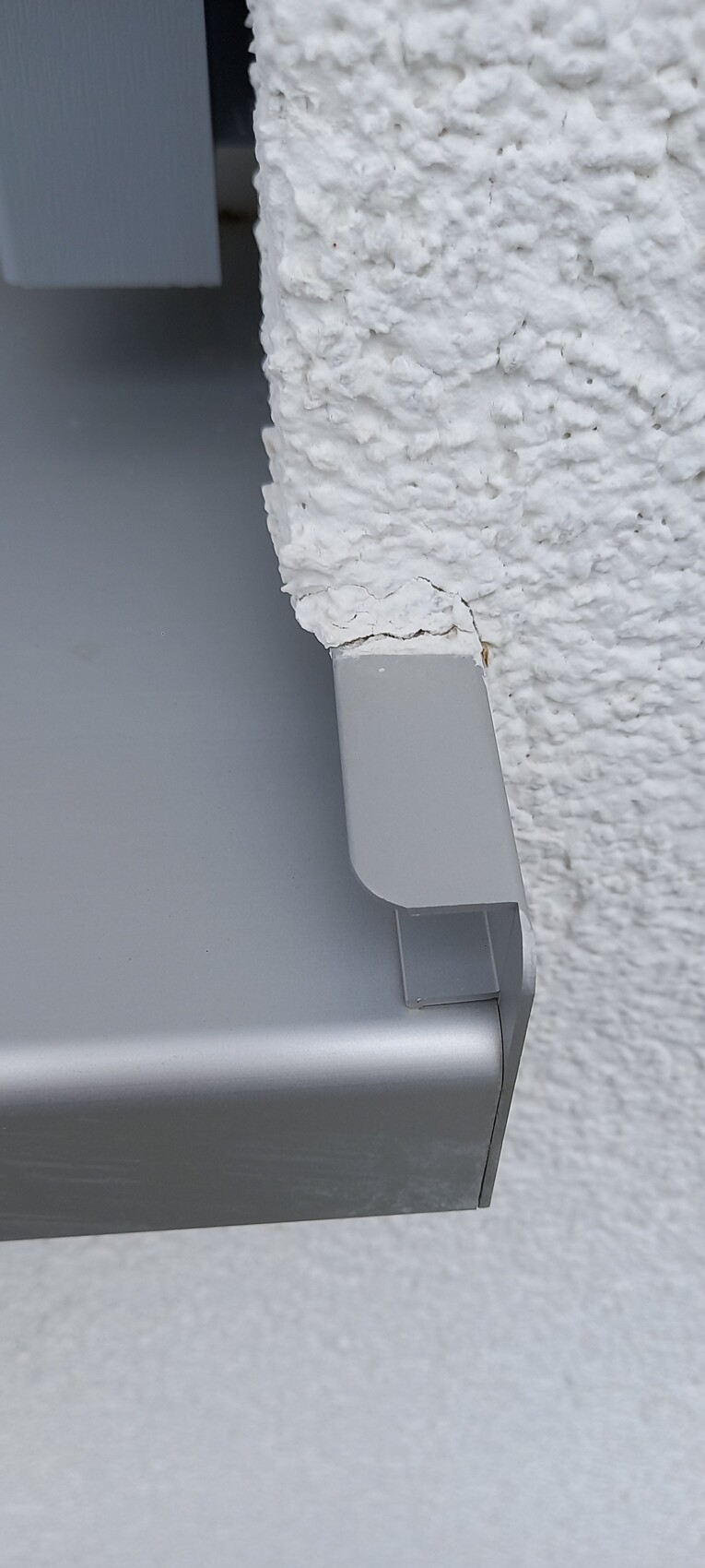 Weiße raue Putzwand mit grauer Metallverkleidung an der unteren Gebäudekante