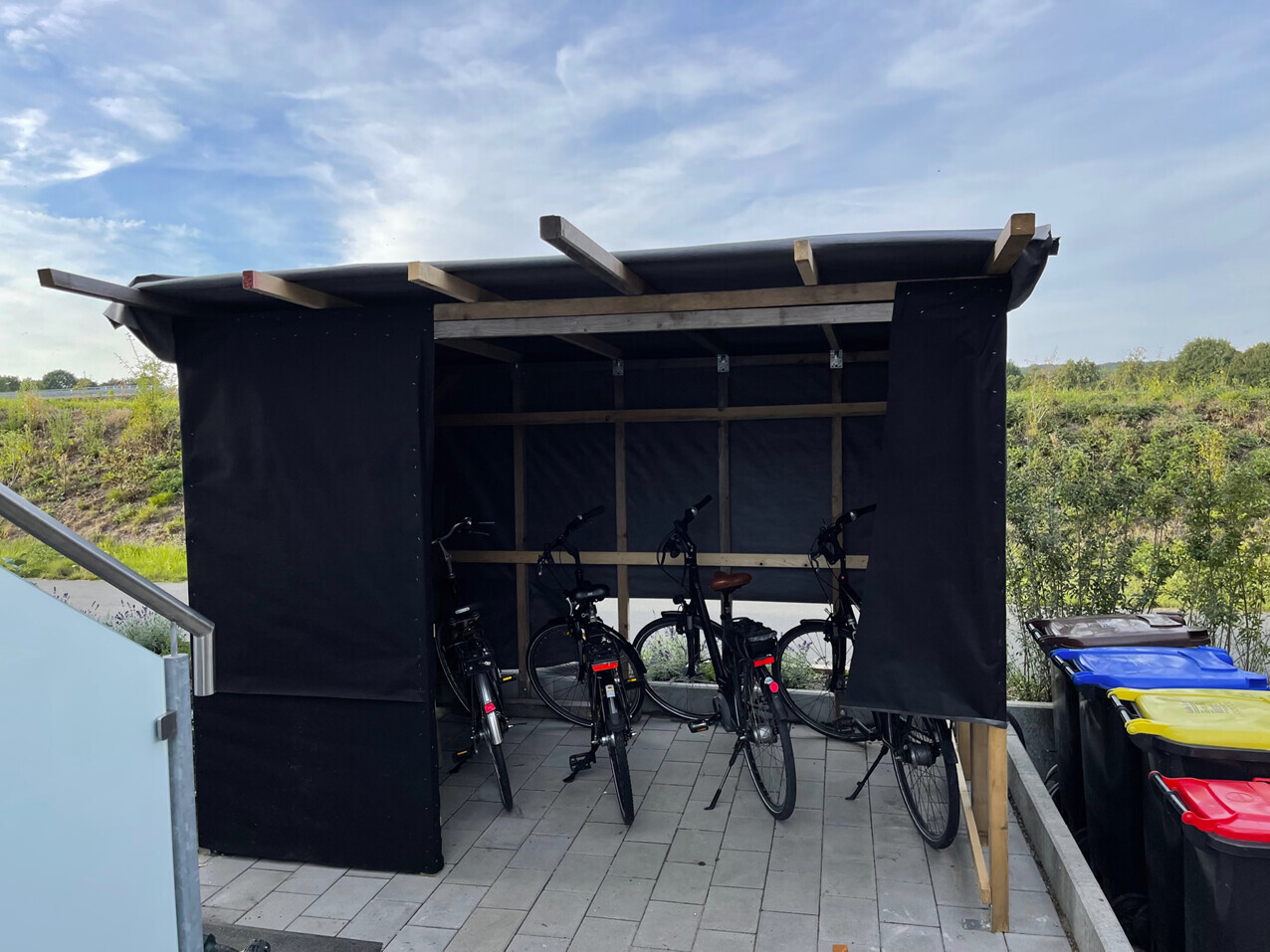 Bike shed made of black fabric with several bicycles on paved ground.