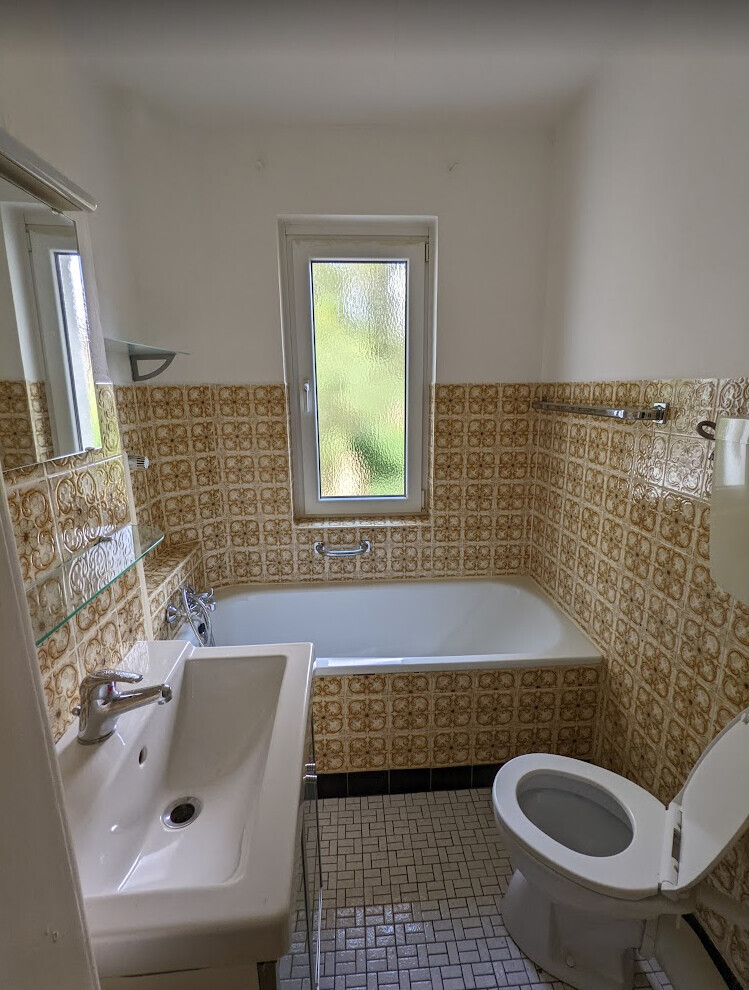 Small bathroom with sink, toilet and bathtub; brown patterned tiles.