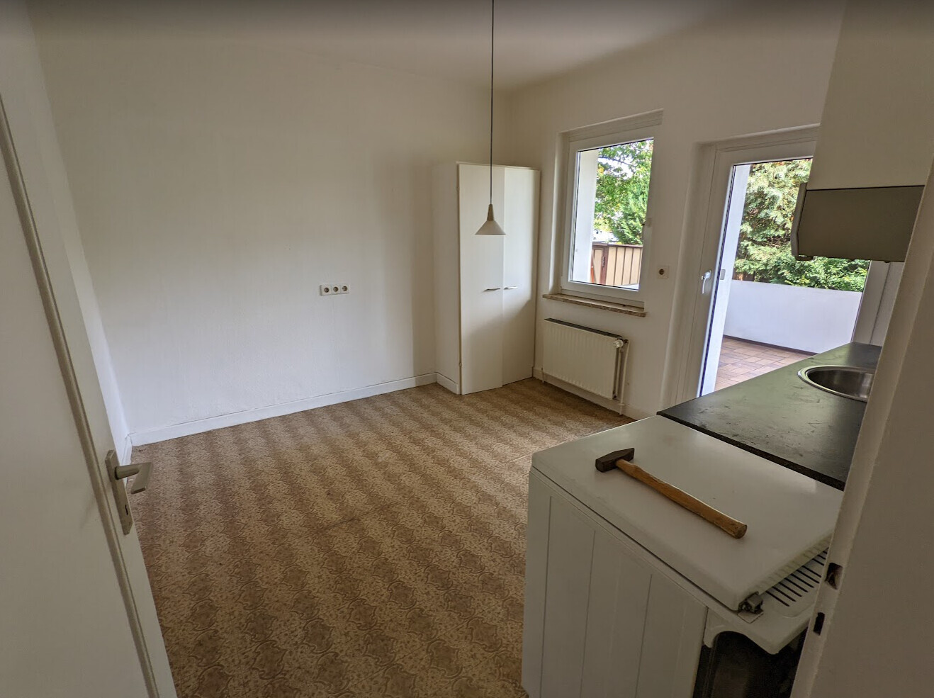 Empty room with beige carpet, white cabinet, window and door to balcony, axe on kitchen cabinet