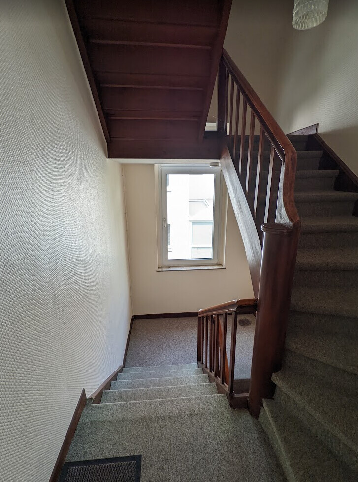 Stairwell with wooden stairs, wooden railing and window at the landing.