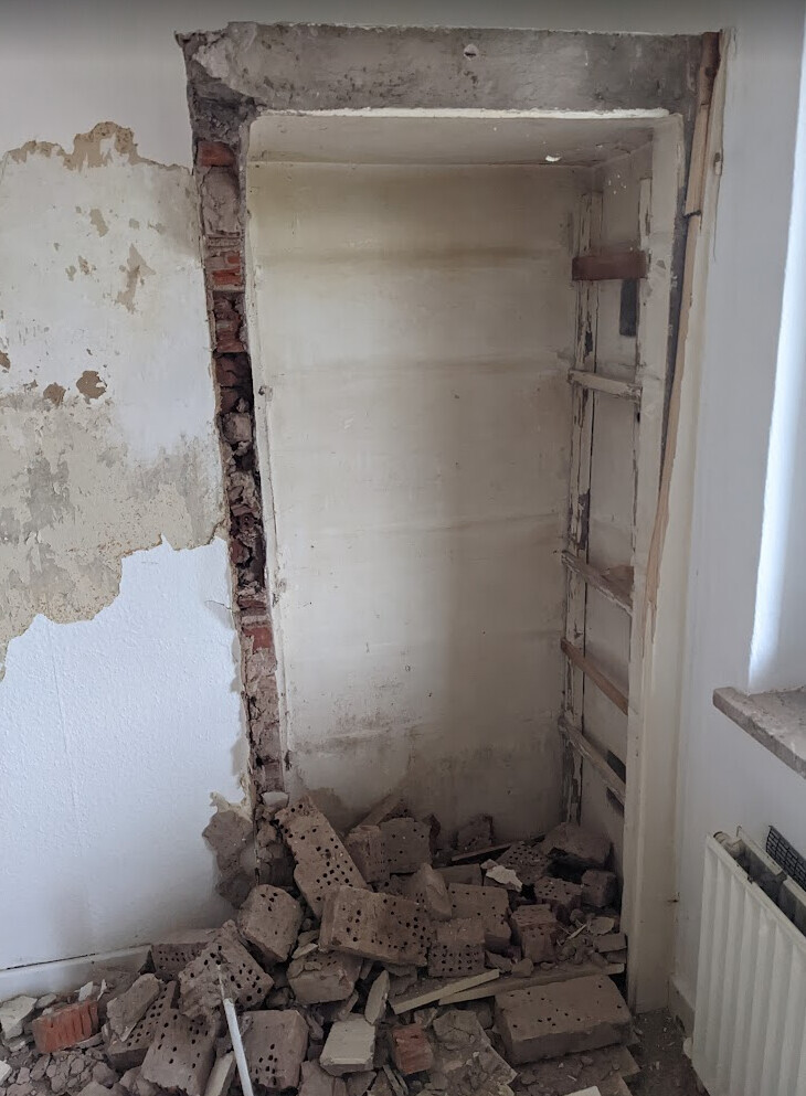 Offene Wandnische mit Bruchziegeln, Schutt am Boden; Heizkörper rechts sichtbar.