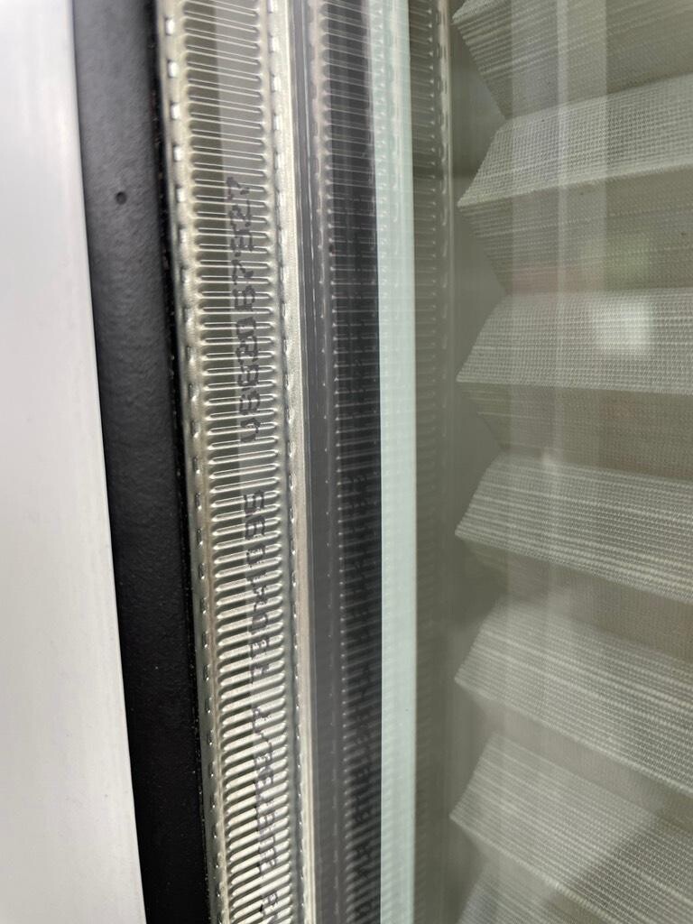 Close-up of a window frame with glass, seal, and horizontal blinds behind.