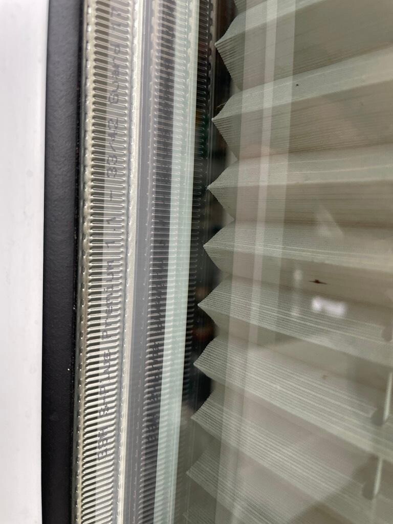 Close-up of a window: on the right a white pleated blind, on the left metal frame.