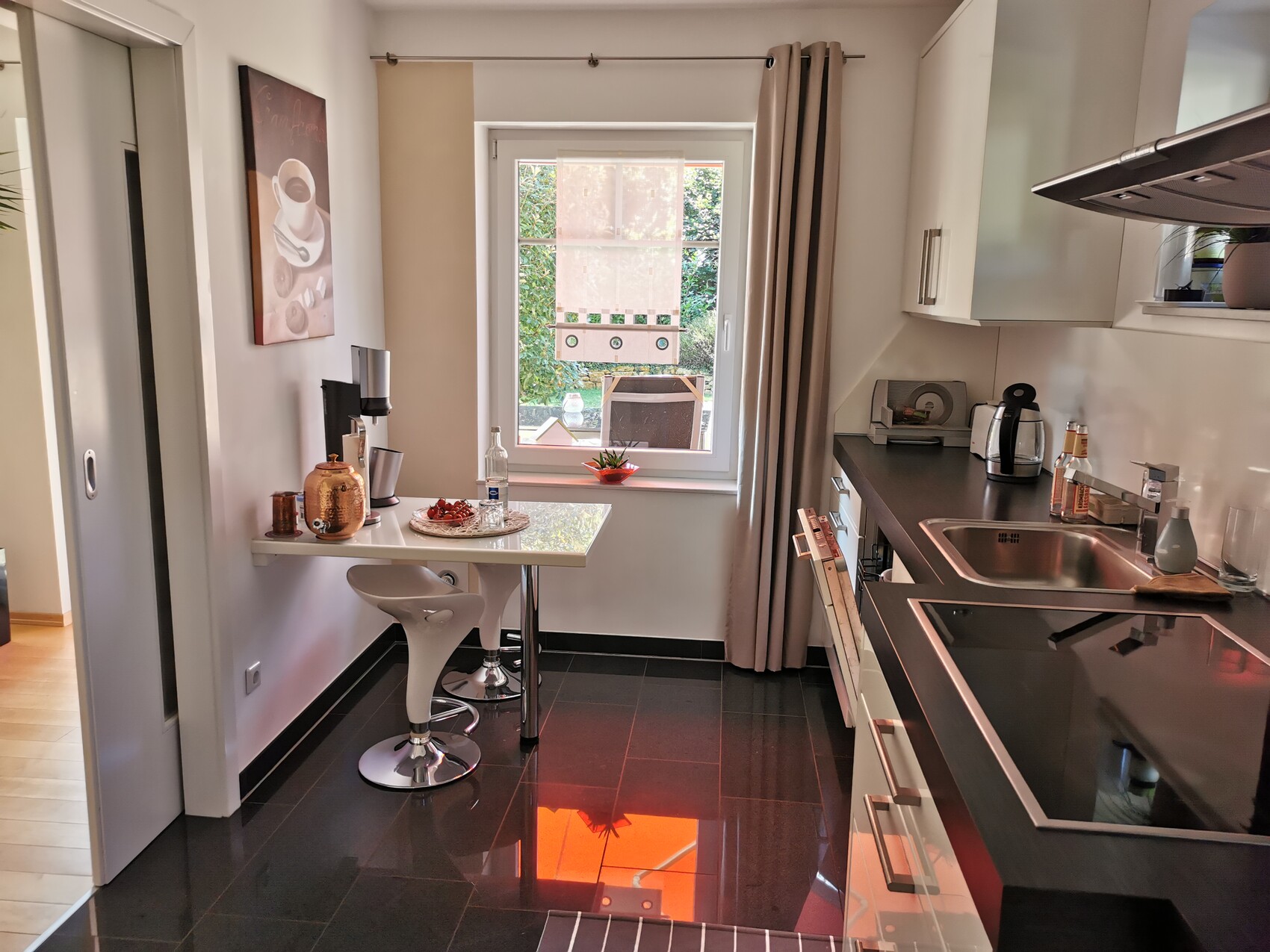 Kitchen unit with window, small dining table, chairs, coffee machine, sink, and stove.