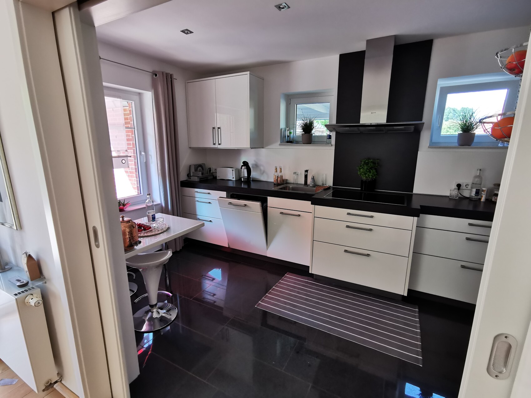 Modern kitchen with white cabinets, black countertop, range hood, and window plants.