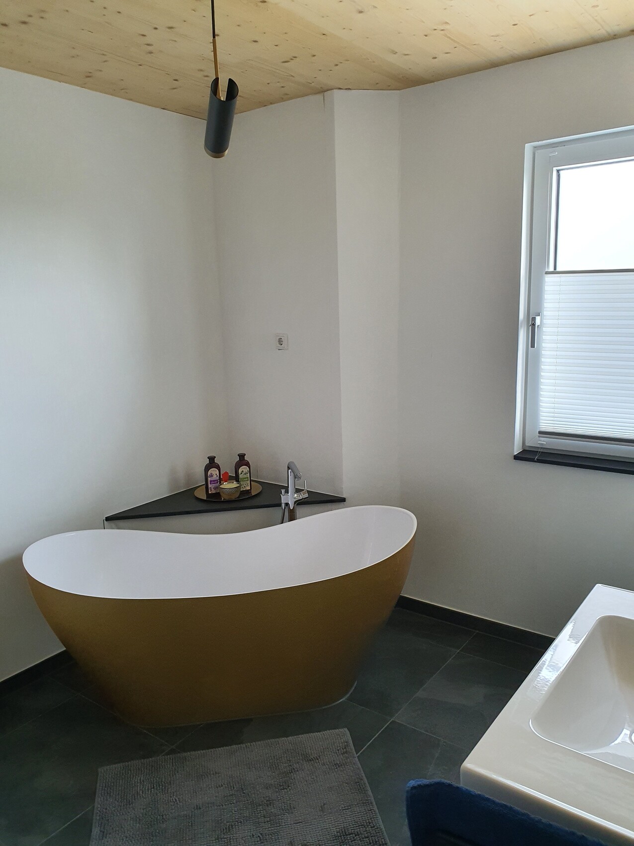 Freestanding gold bathtub with white interior, corner with care products, window with shutter