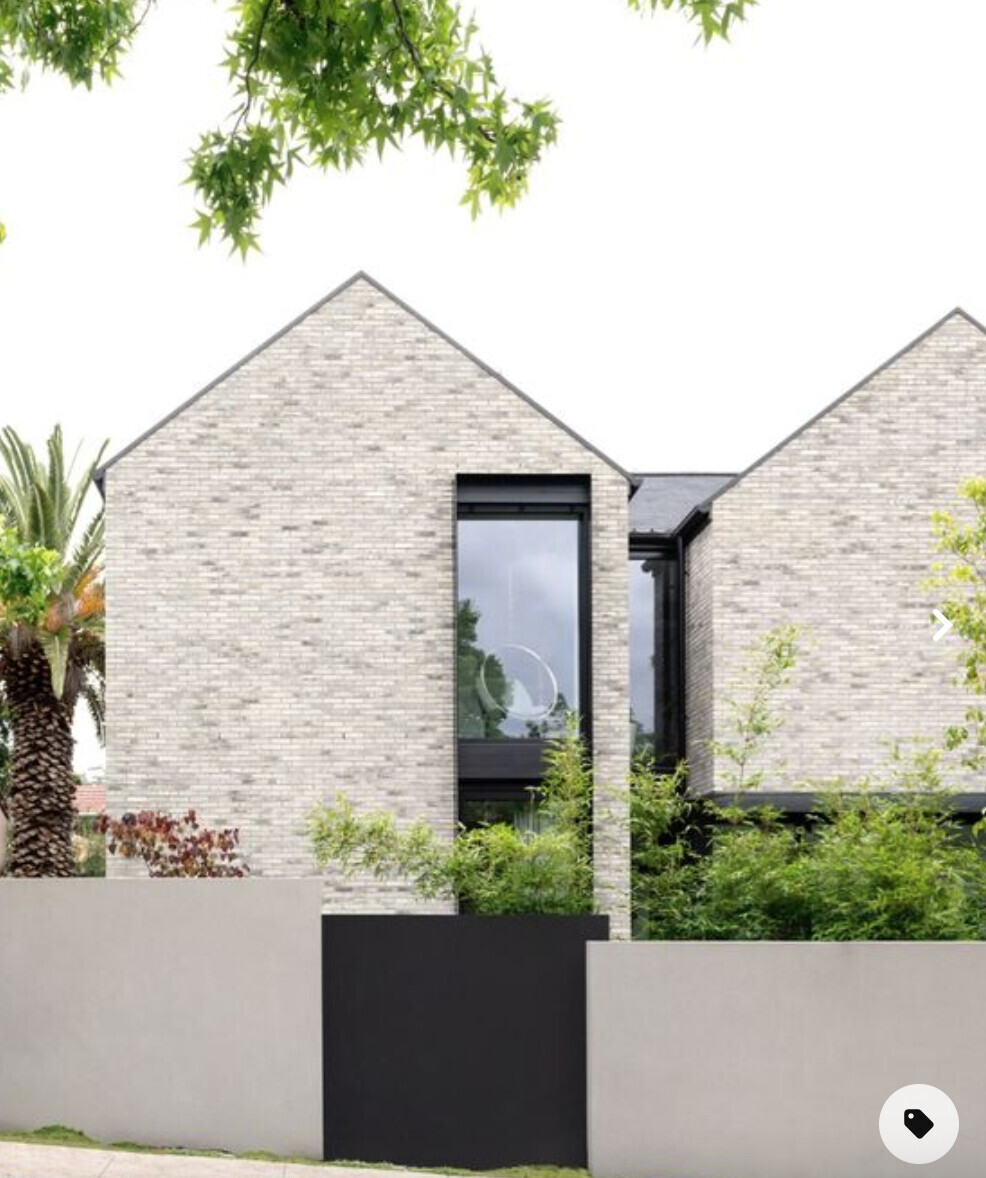 Modern brick villa with large windows, surrounding greenery, and gray wall.