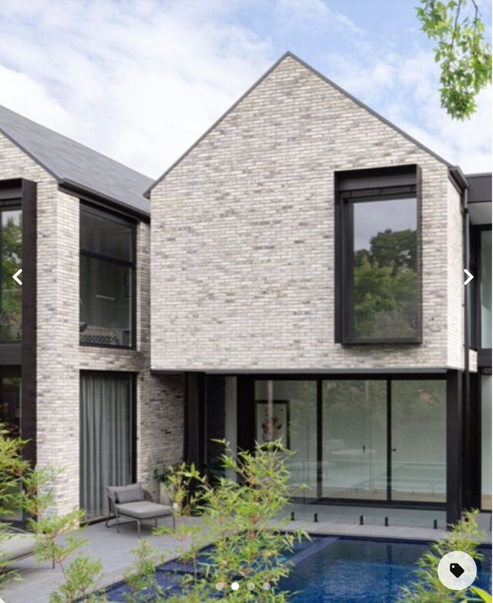 Modern villa-style house front made of light brick, large glass fronts, pool in the front yard.