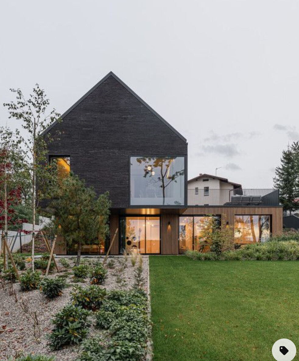 Modern two-story house with black brick facade and large windows facing the garden.