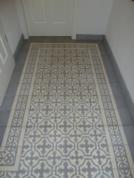 Hallway with light gray ornamental tiles, wide border pattern; door in the background.