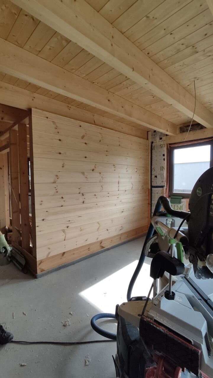 Interior of a wooden house under construction, wooden walls, ceiling beams, window and circular saw.