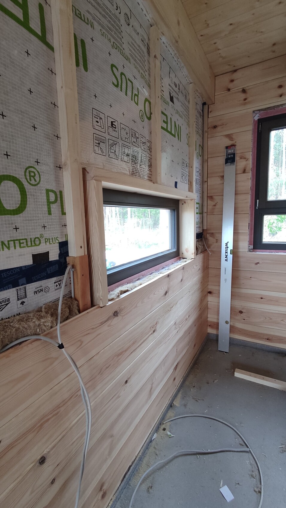 Interior of a wooden house under construction: window, wood cladding, insulation, spirit level.
