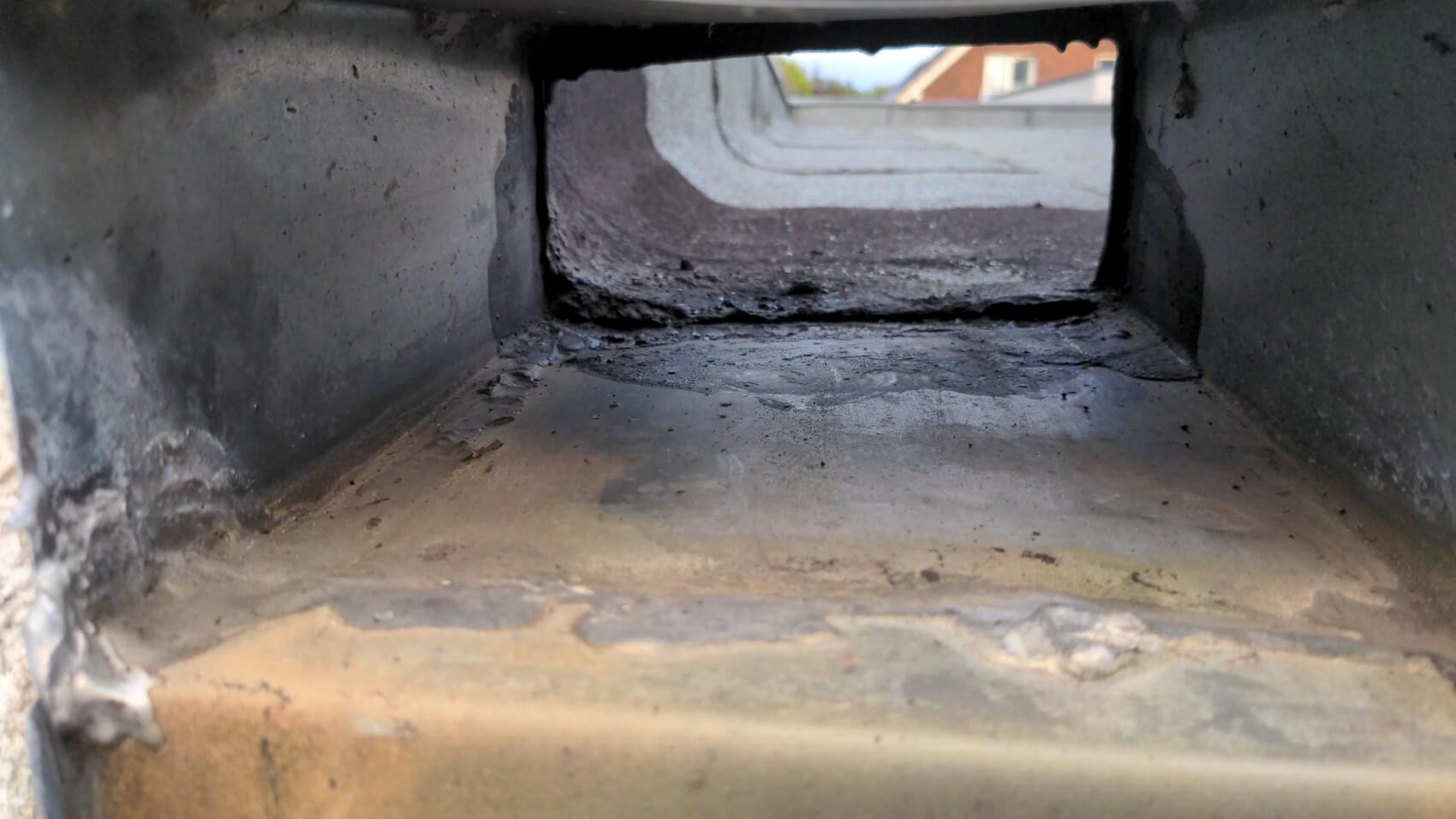 Darker, soot-stained rectangular interior channel; view through opening to roof tiles outside.