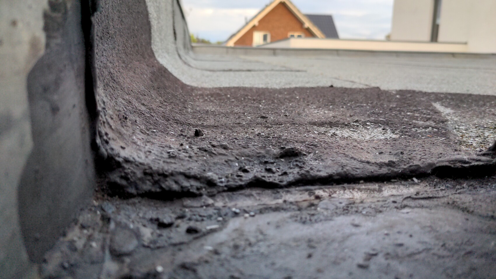 Close-up of a bitumen-covered roof edge with tar residue; houses in the background.