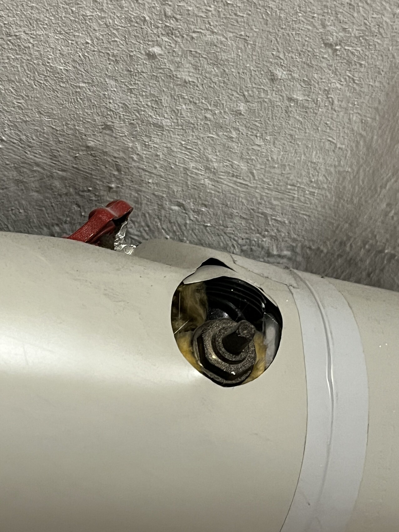 Close-up of a white pipe with an open end; a screw head/bolt and red cable are visible behind it.