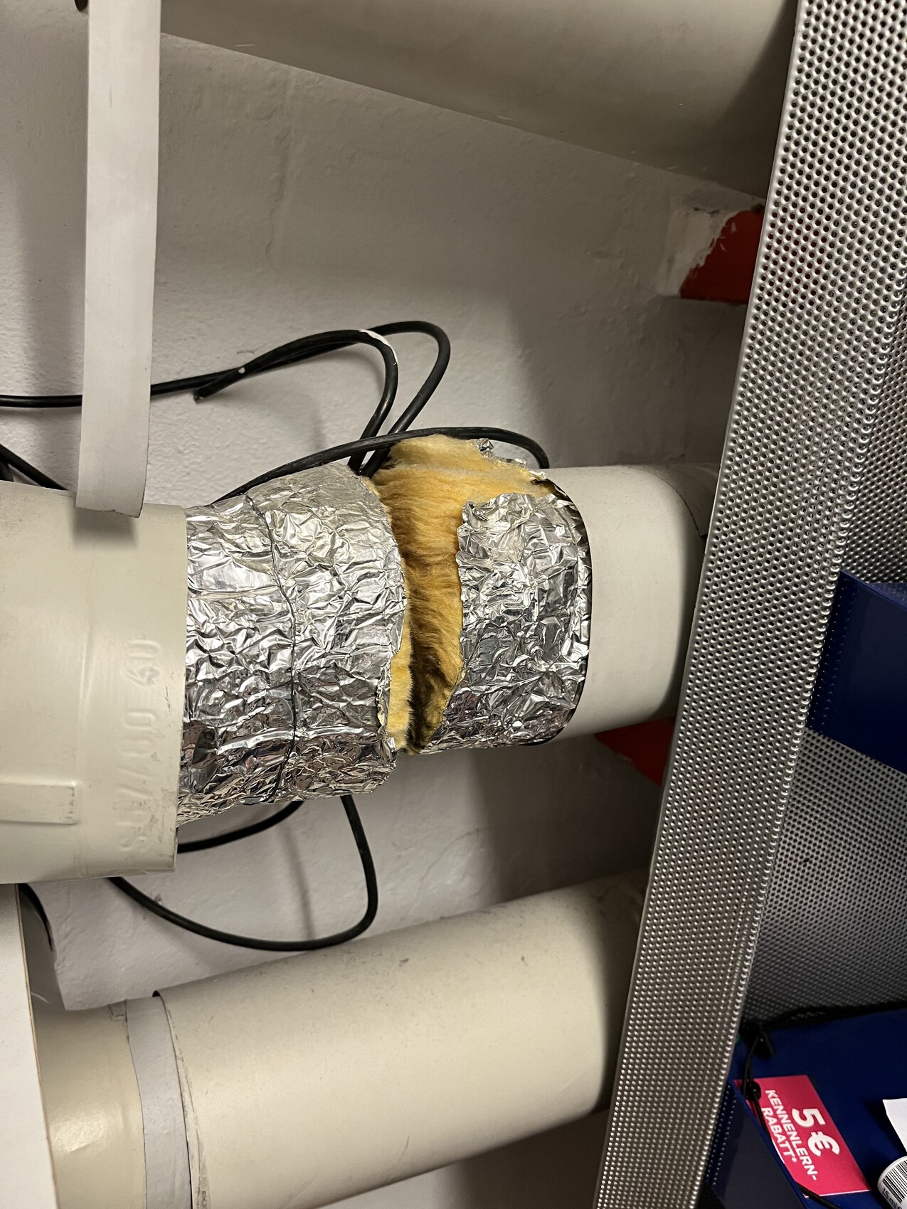 Insulated pipe with yellow insulation wrapped in aluminum foil, cable next to it.