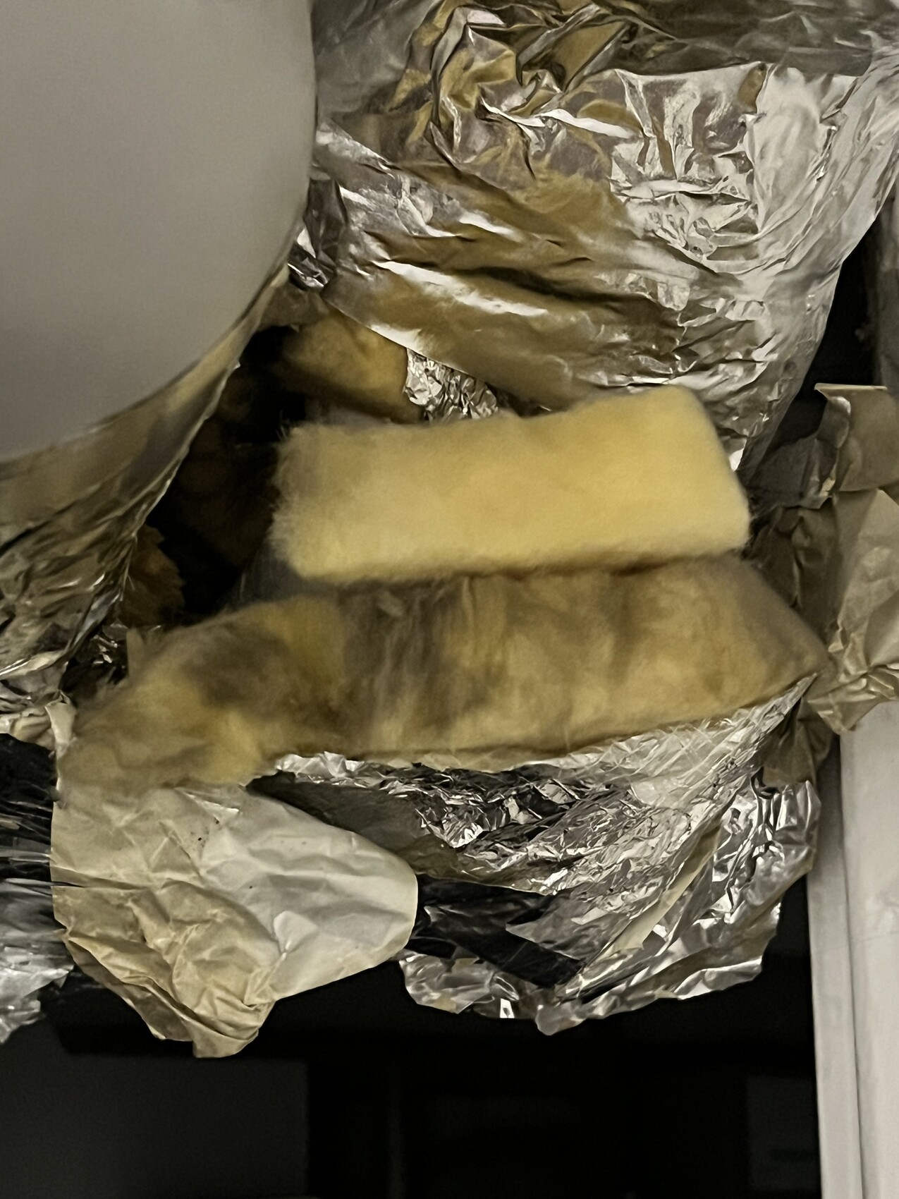 Ventilation shaft with crumpled aluminum foil and yellow insulating wool.