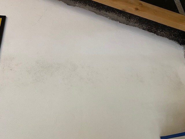 White wall with gray damp spots; wooden beams and a dark edge at the top.