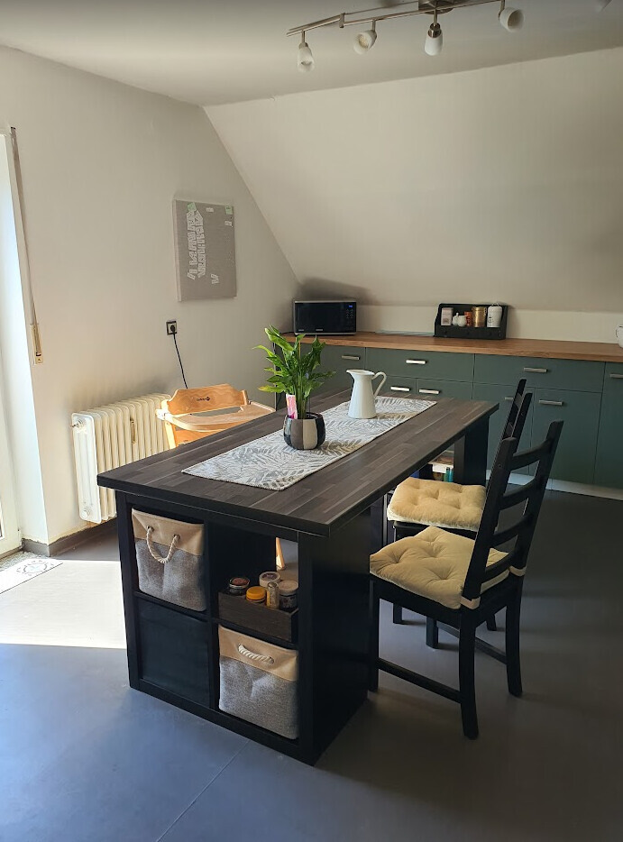 Modern kitchen with dark table island, baskets underneath, plant and kitchen line in the background.