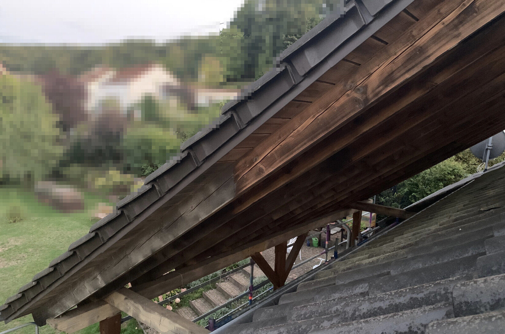 Top view of a wooden roof with rafters, roof tiles, and scaffolding in the garden.