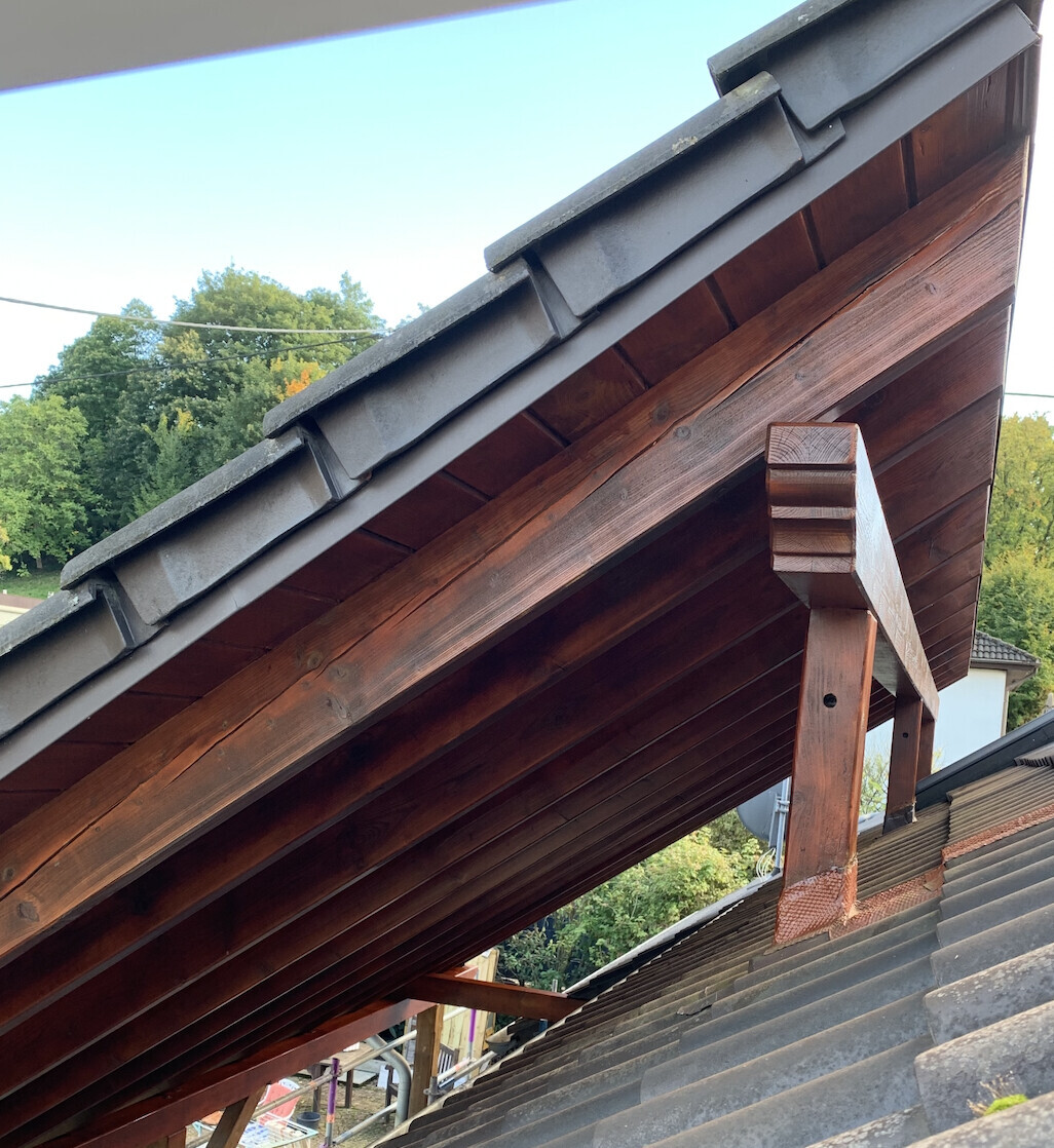 Substructure of a wooden roof with dark beams and gray roof tiles, view from below.