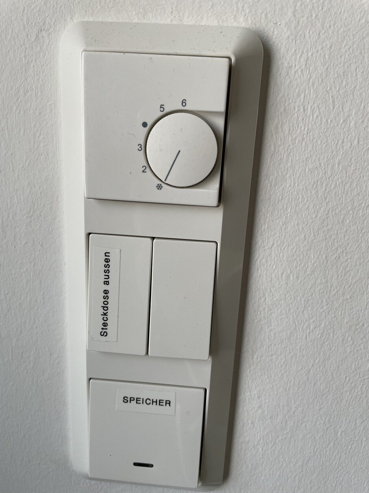 Wall panel with thermostat rotary knob at the top, two switches, stickers labeled 'Outdoor socket' and 'WATER HEATER'.