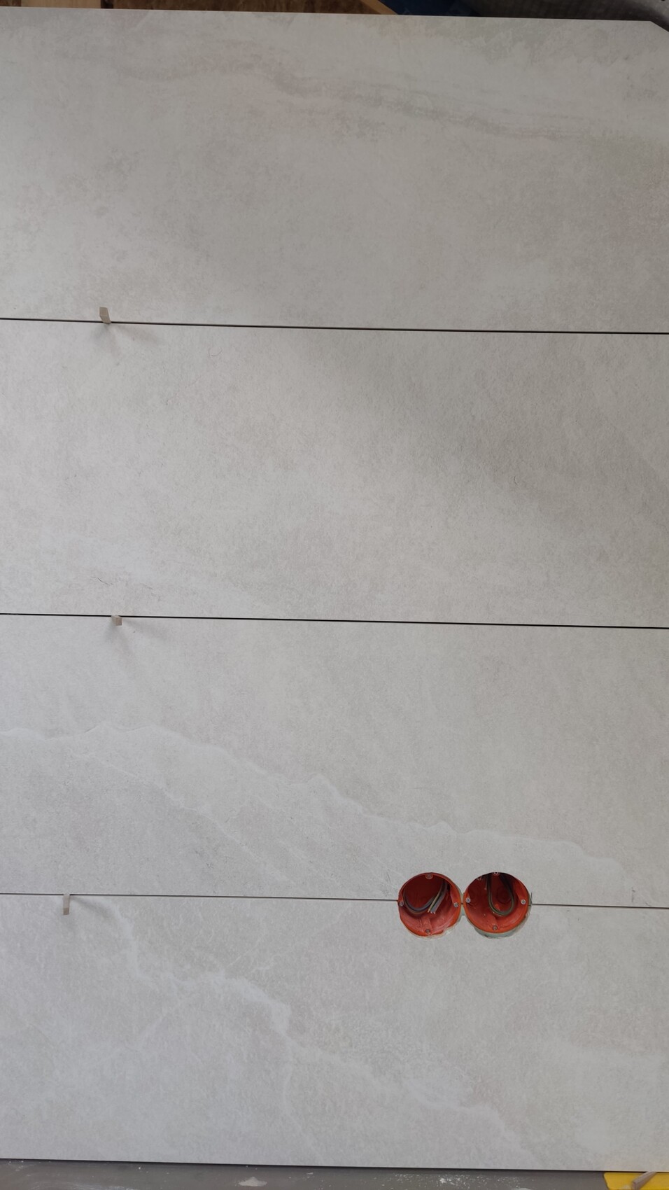 Large light gray tiles with grout lines, two red round electrical installation boxes.