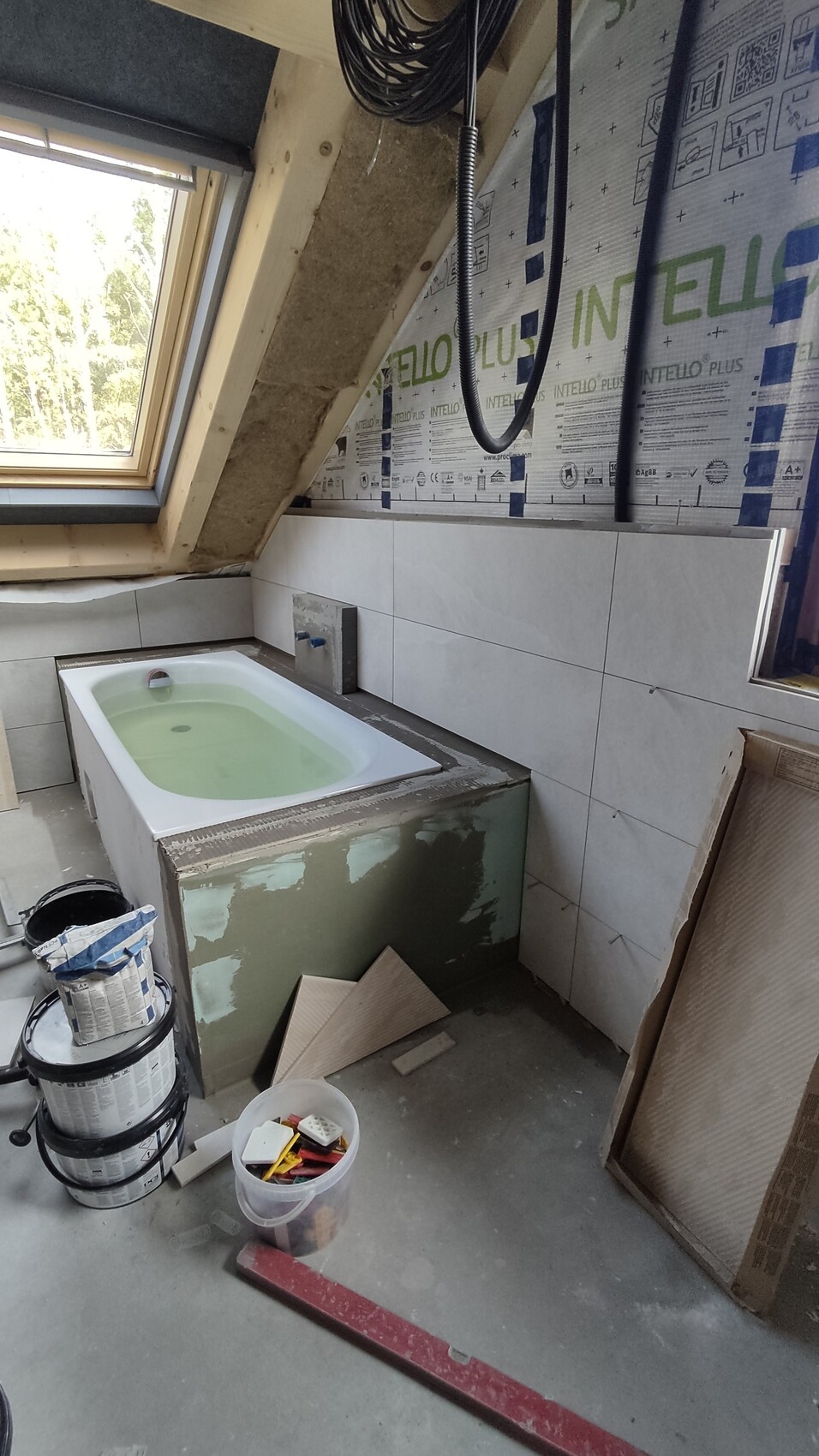 Bathroom under construction with exposed insulation, bathtub, tiles, and building materials.
