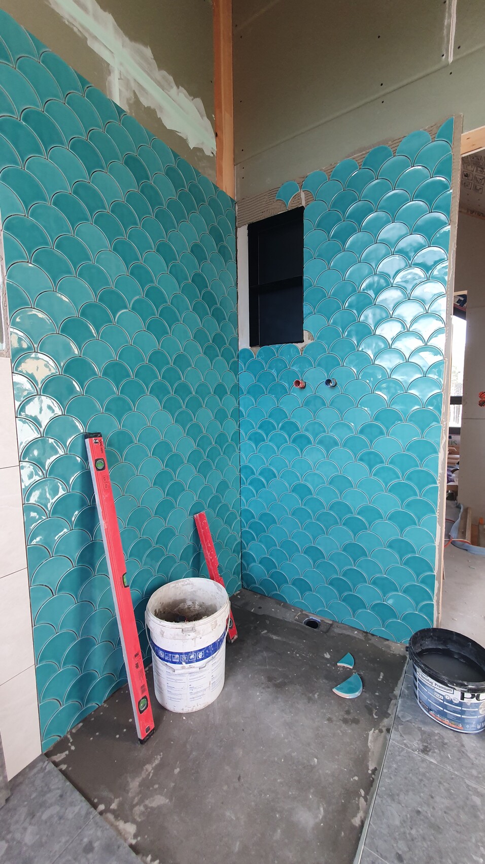 Turquoise fish scale tiles on wall, construction tools and bucket on site.