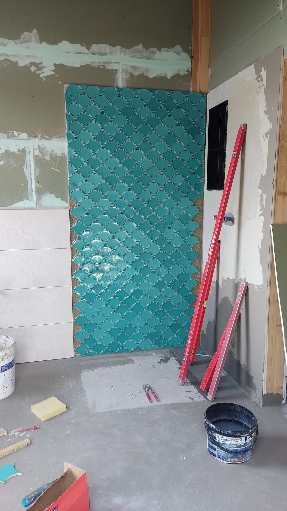 Teal-colored herringbone/fish scale tiles on wall in construction area, red ladder, construction tools.