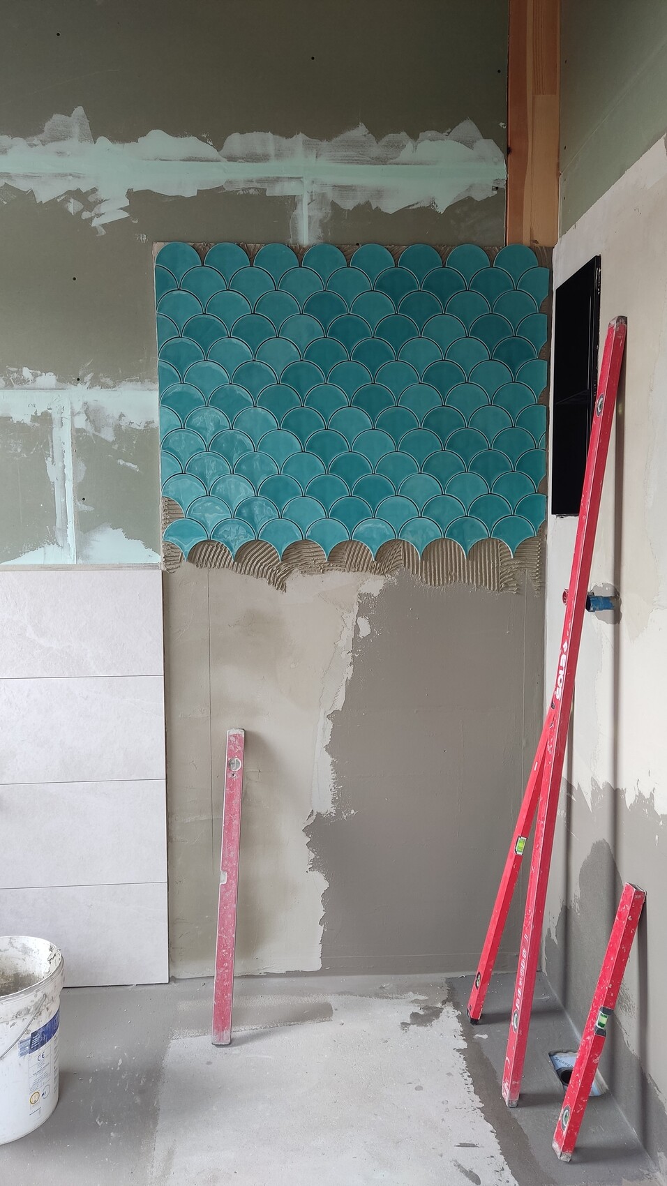 Rough construction site with blue-green fish scale tiles on the wall; red ladder and construction tools in the room.