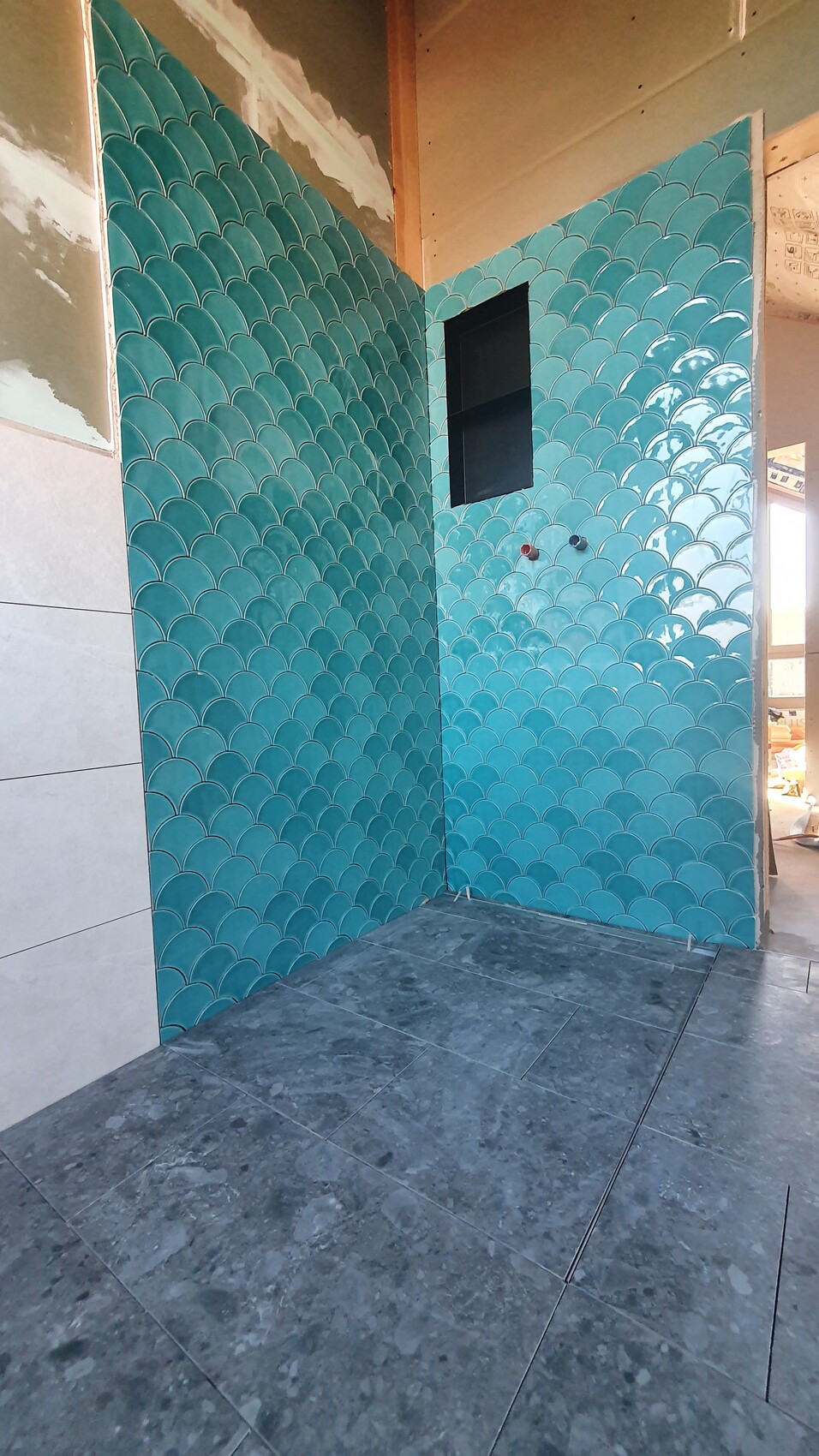 Turquoise-green fish scale tiles on the walls; small black window opening, visible water connections.