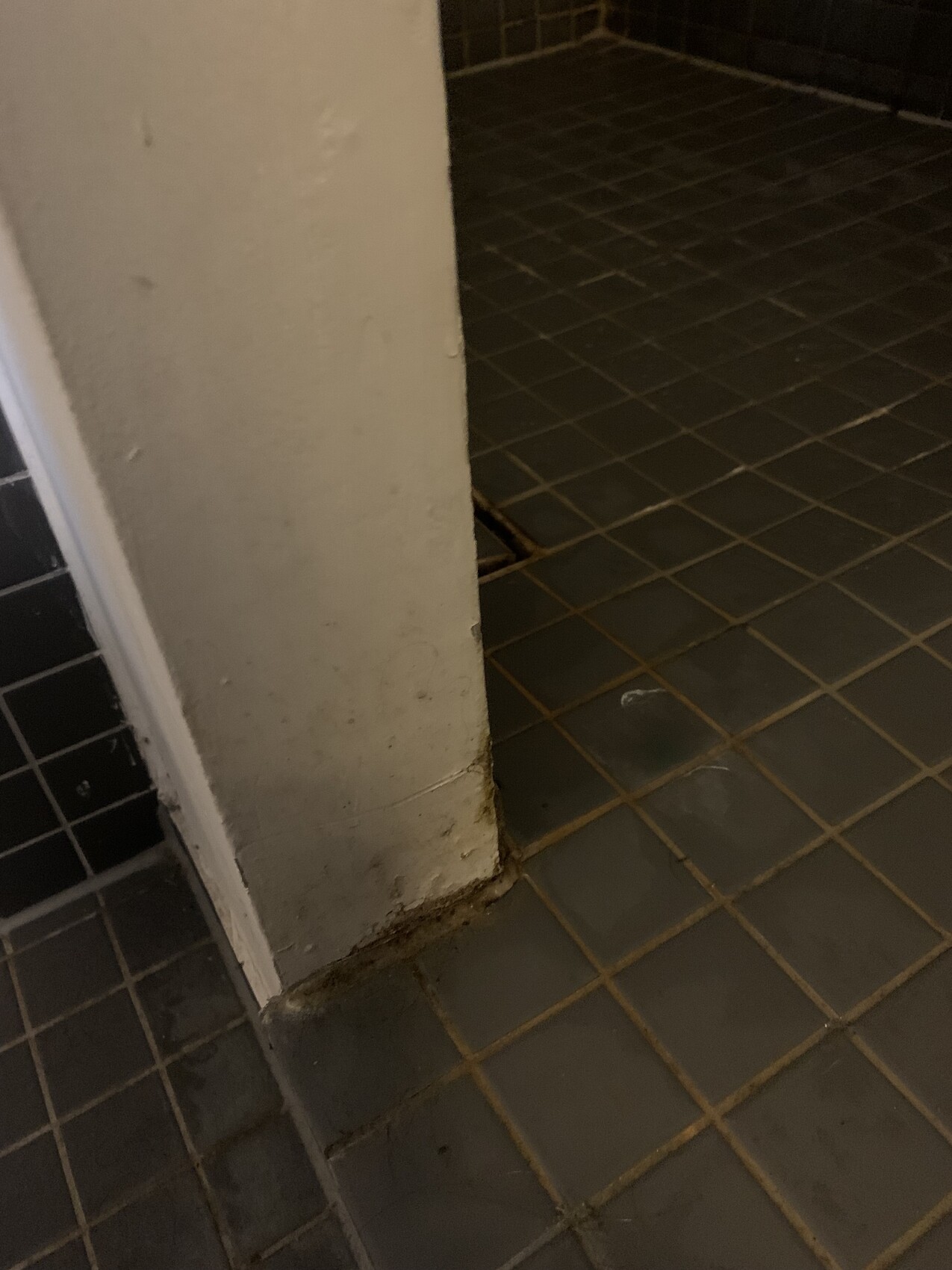 White wall column next to gray tiles, dirty floor edge.