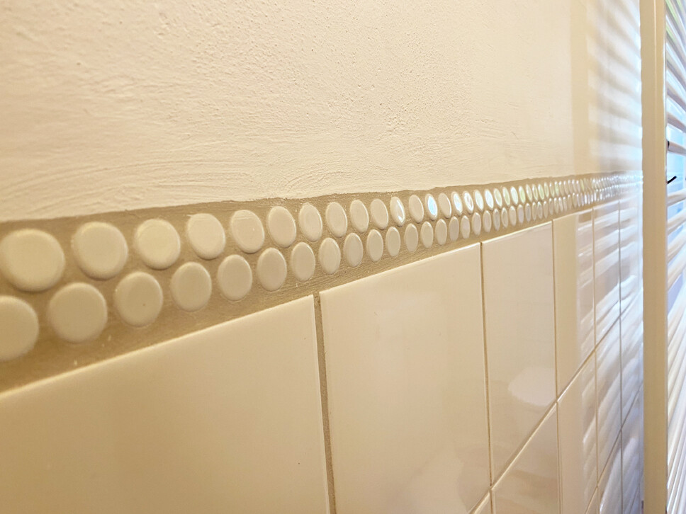 Wall with a decorative strip of white, round buttons above tiles.