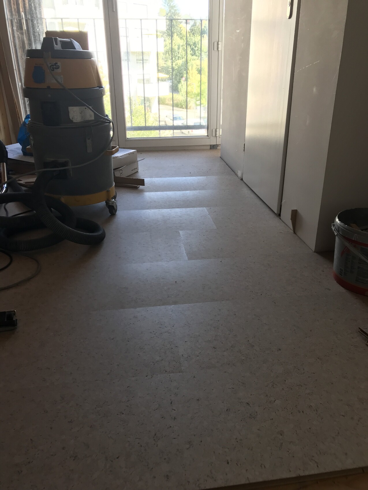 Renovation room with vacuum cleaner, hose, bucket, and balcony door in the background.