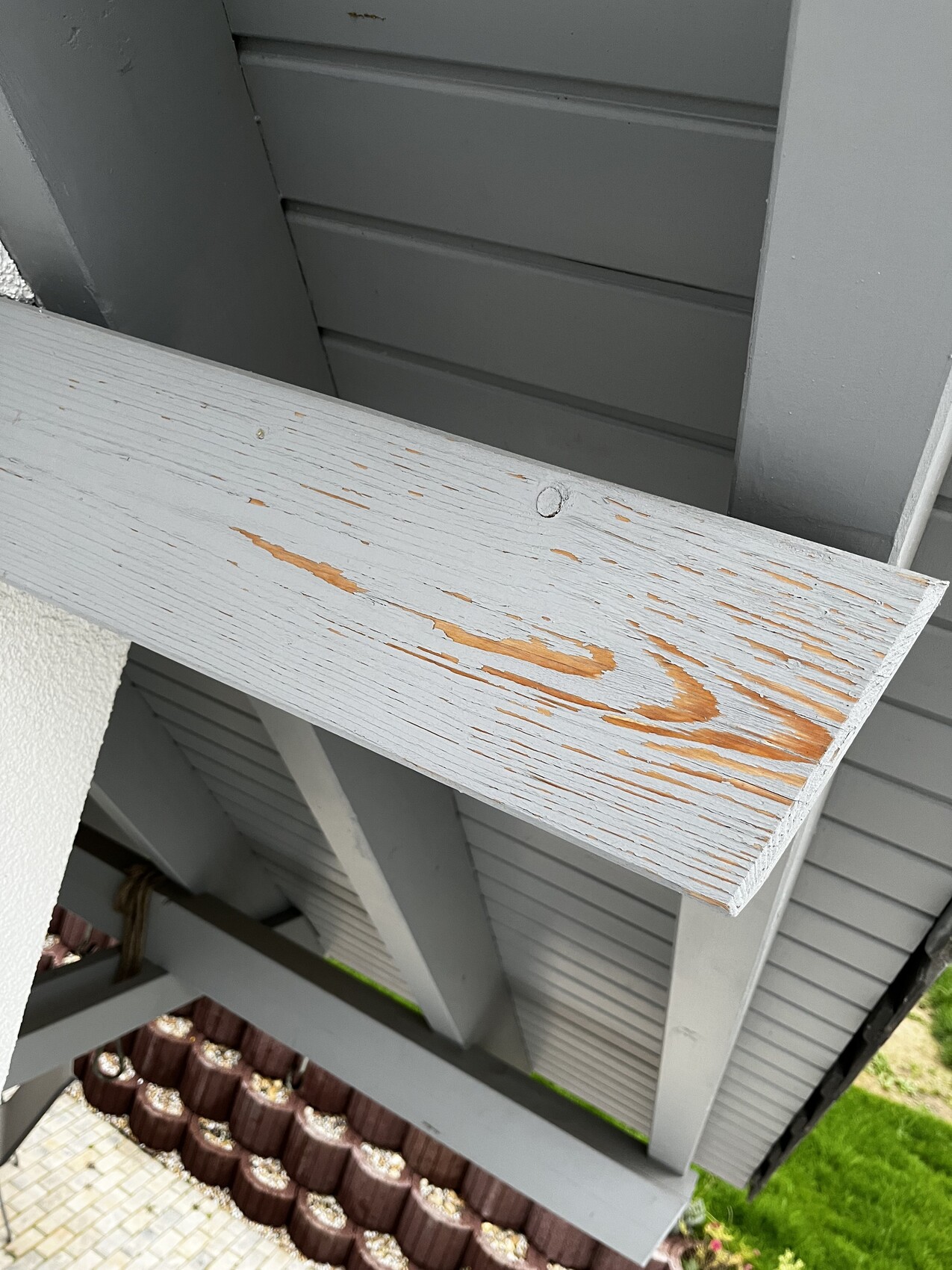 Wooden beams with peeling gray paint; below, orange-colored wood.