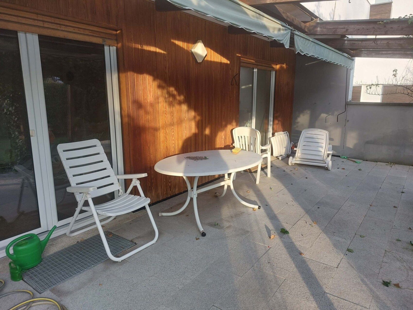 Terrace with white plastic chairs, round table, and loungers in front of a wooden wall.